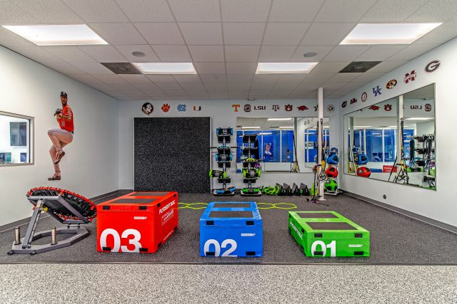 Athletic training facility with color-coded plyometric boxes, rubber flooring, wall-mounted equipment storage, floor-to-ceiling mirrors, and collegiate sports branding