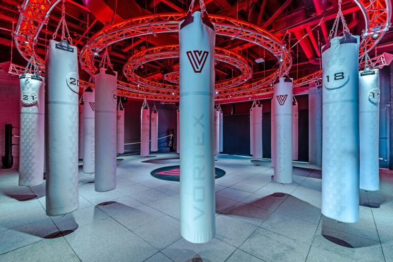 Fitness and athletic facility buildout by Construction Concepts featuring branded heavy bags, circular truss lighting, and dramatic red accent lighting