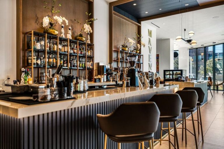 Upscale bar and restaurant buildout by Construction Concepts featuring a marble bar top, fluted paneling, backlit liquor shelving, and leather barstools
