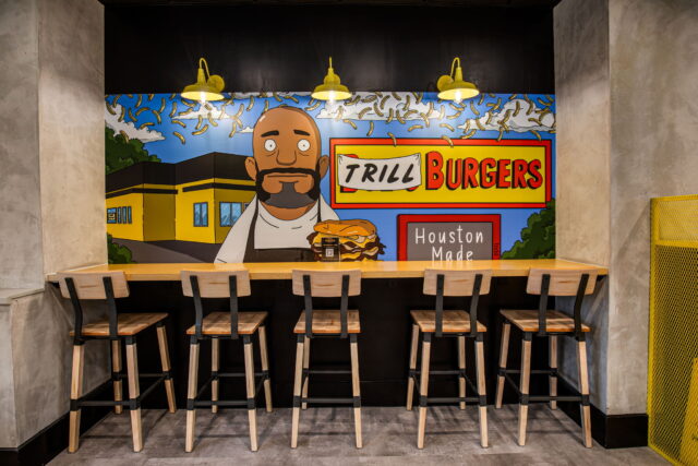 Trill Burgers restaurant interior with counter seating, bar stools, and a bold Houston-themed cartoon mural